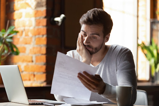 Young man looking stressed while sitting at desk reading letter 