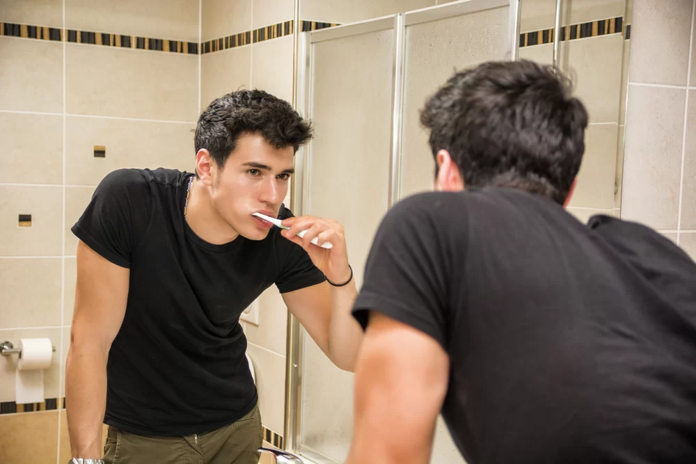 Man brushing his teeth while looking in bathroom mirror