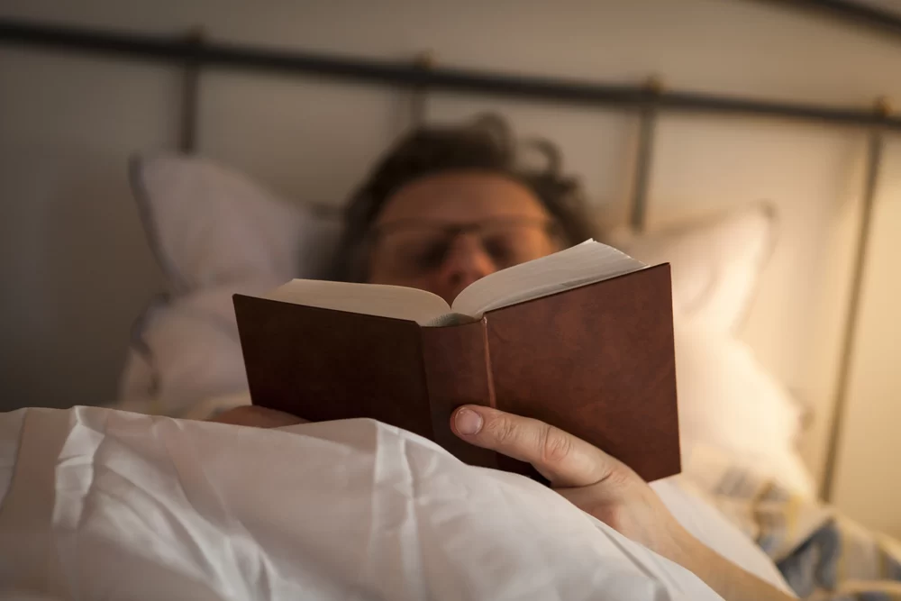 Man in glasses reading a book in bed