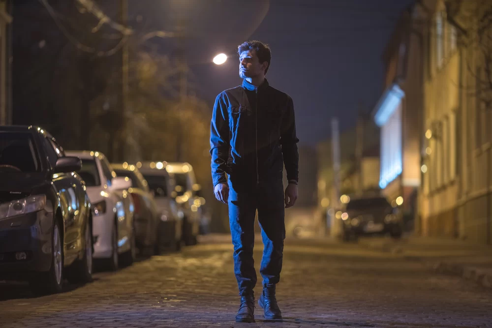 Man wearing jacket walking down city street at night