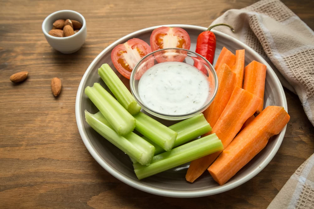 Tray of raw vegetables with dip and bowl of almonds on table