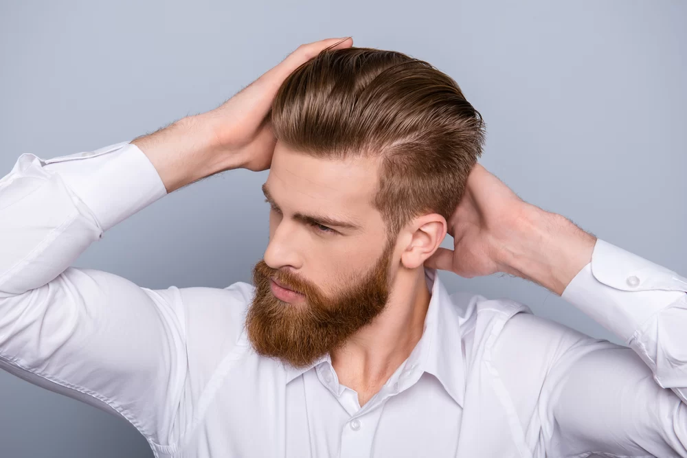 Confident, stylish man with red beard running his hands over his hair