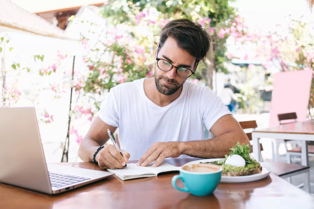 Man sitting outside at table making notes while eating dinner