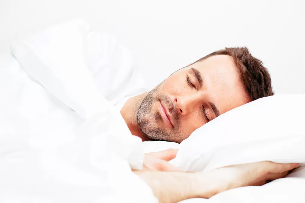 Man sleeping peacefully on bed with white bedding