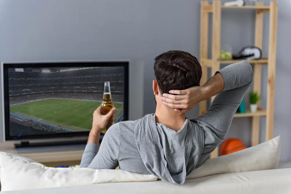 Man watching sports on television while relaxing on the couch and drinking a beer