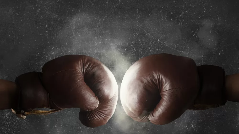 Two boxing gloves hitting each other in ring of dust and light