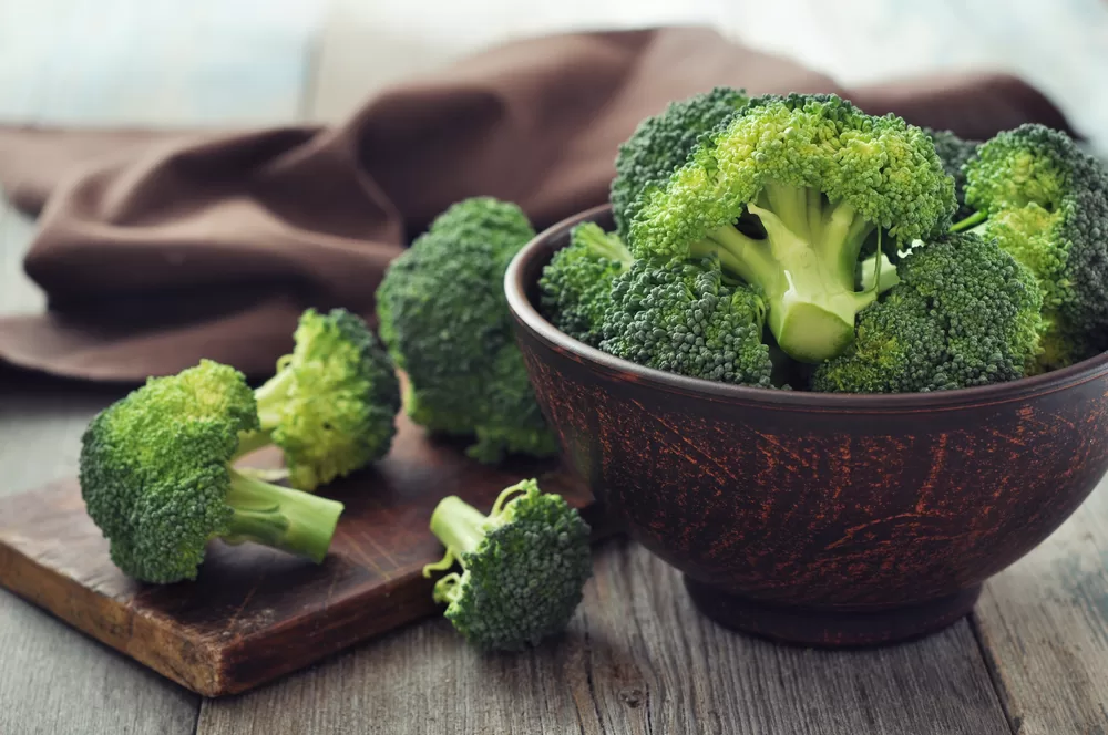 Bowl of cut broccoli on wooden table