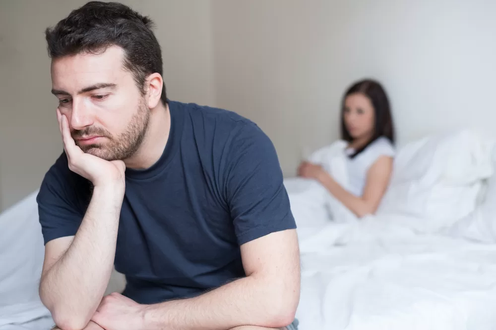 Frustrated man sitting in bed with wife